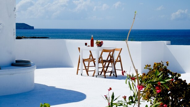 A white outdoor seating area with a table and chairs, overlooking a clear blue sea. - Roof garden Seaside lux Home (Chania)