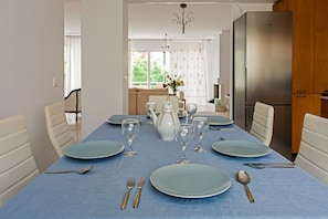 Un coin repas avec une nappe bleue, des chaises blanches et un réfrigérateur en acier inoxydable.