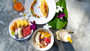 A tropical breakfast spread on a stone table with a banana, mango, red fruit, and a bowl of mixed berries and nuts. - Lazy Day The Resort (Ko Mak)