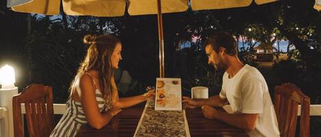 Two people seated at a wooden table under a large umbrella, with a menu in front of them.