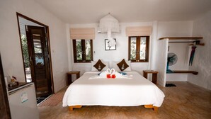 A bedroom with a large bed, two bedside tables, a ceiling fan, and a window with a view of greenery. - Lazy Day The Resort (Ko Mak)