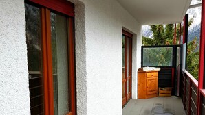 Un couloir avec un banc en bois, une petite armoire en bois et une porte vitrée donnant sur un balcon avec vue sur les arbres.