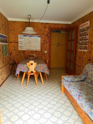Una habitación pequeña con una mesa y sillas de madera, una cama y un mapa en la pared.