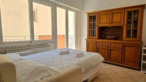 A bedroom with a bed, a wooden cabinet with glass doors, a television, and a window with a view of the outside. - Monterosso Apartment (Monterosso al Mare)
