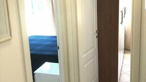 A hallway with a white door leading to a room with a bed and a window. - Monterosso Apartment (Monterosso al Mare)