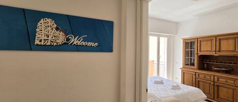 A bedroom with a bed, a wooden cabinet, and a blue welcome sign.