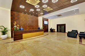 A reception area with a wooden reception desk, a flat-screen TV, and a seating area with sofas. - Manpho Bell Hotel & Convention Center (Bengaluru)