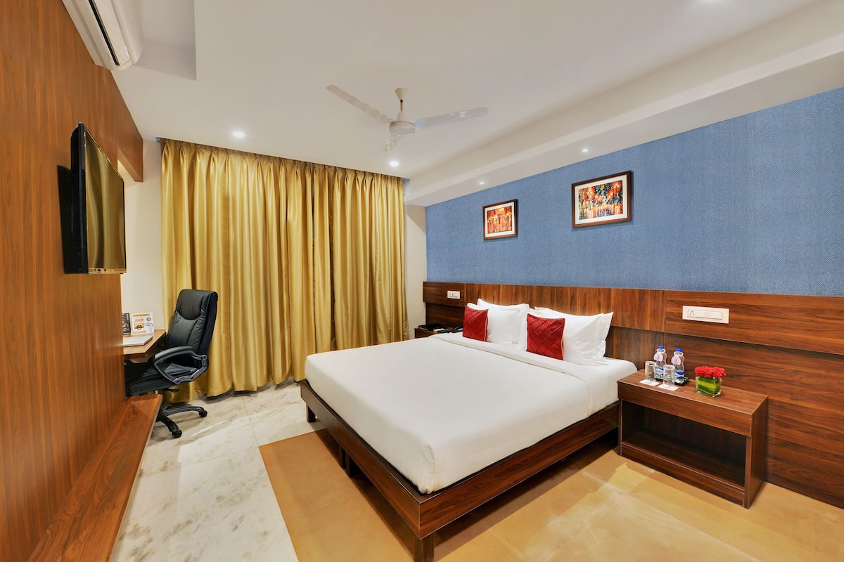 A hotel room with a large bed, a desk with a chair, a nightstand, and a ceiling fan.