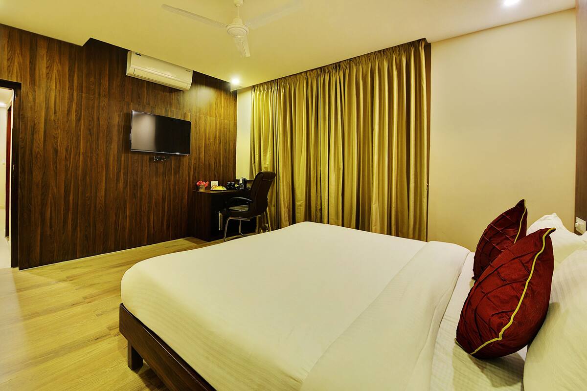 A hotel room with a bed, a desk with a chair, a television, and a window with curtains.