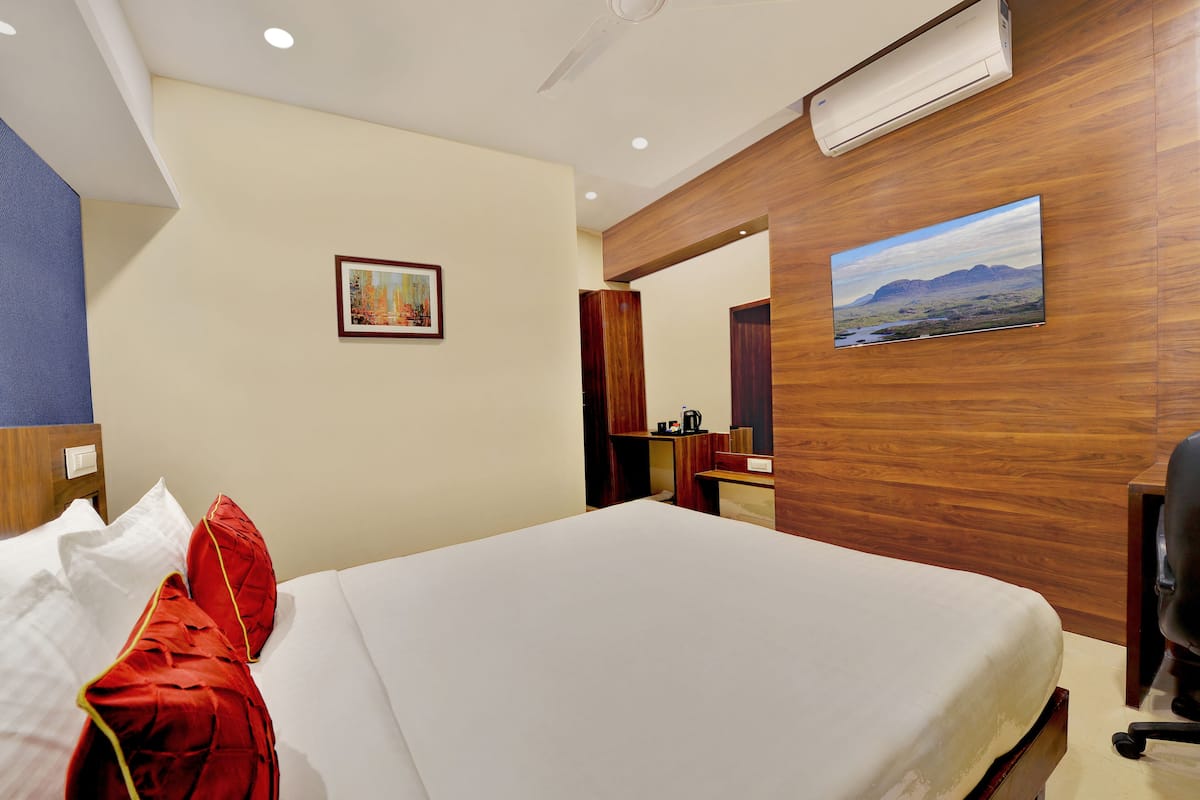 A hotel room with a bed, a painting on the wall, a wooden cabinet, and a desk with a chair.