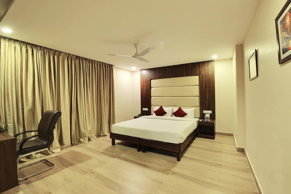 A hotel room with a bed, a desk, a chair, a nightstand, a ceiling fan, and curtains.
