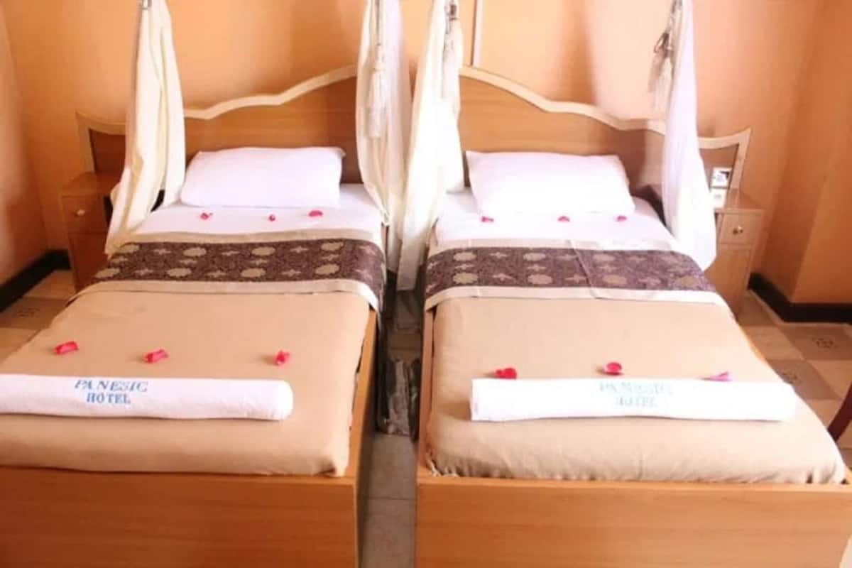 Deux lits jumeaux avec des baldaquins, chacun agrémenté d’un oreiller et d’une serviette portant le nom de l’hôtel.