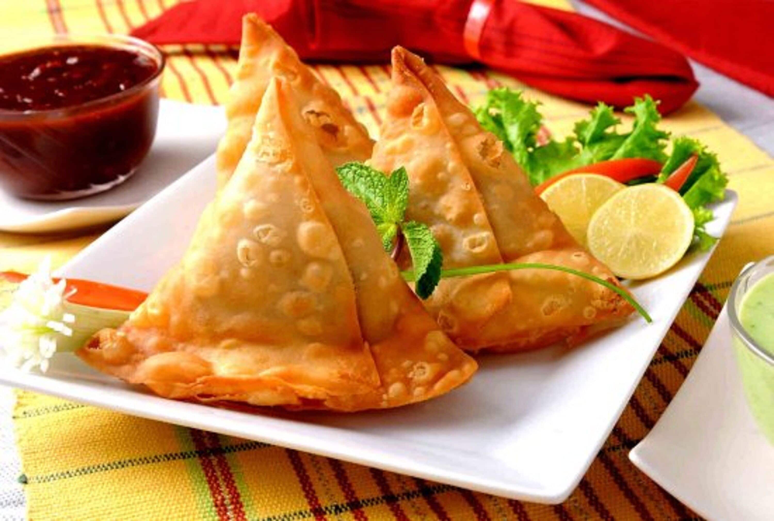 A plate of samosas with mint leaves and a slice of lime.