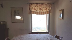 Un comedor con una mesa cubierta con mantel floral, una ventana con cortina floral y dos cuadros en las paredes.