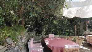 Un patio al aire libre con un muro de piedra, una mesa con mantel a cuadros y sillas con cojines a rayas.
