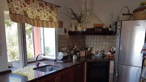 Una cocina con armarios de madera oscura, un refrigerador de acero inoxidable, un horno empotrado y una ventana con cortina floral.
