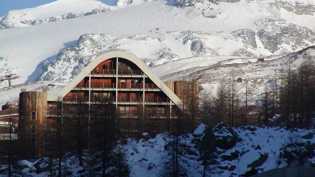 A mountain lodge with a large arched entrance, wooden interior, and a view of snow-covered peaks. - La Grande Ourse (Valtournenche)