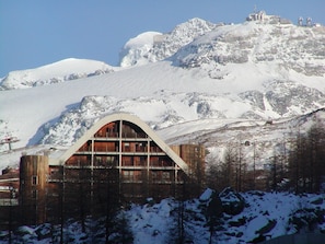 A mountain lodge with a large arched entrance, wooden interior, and a view of snow-covered peaks. - La Grande Ourse (Valtournenche)
