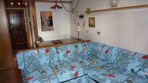 A living room with a sofa, a dining table, and a kitchen area in the background. - La Grande Ourse (Valtournenche)