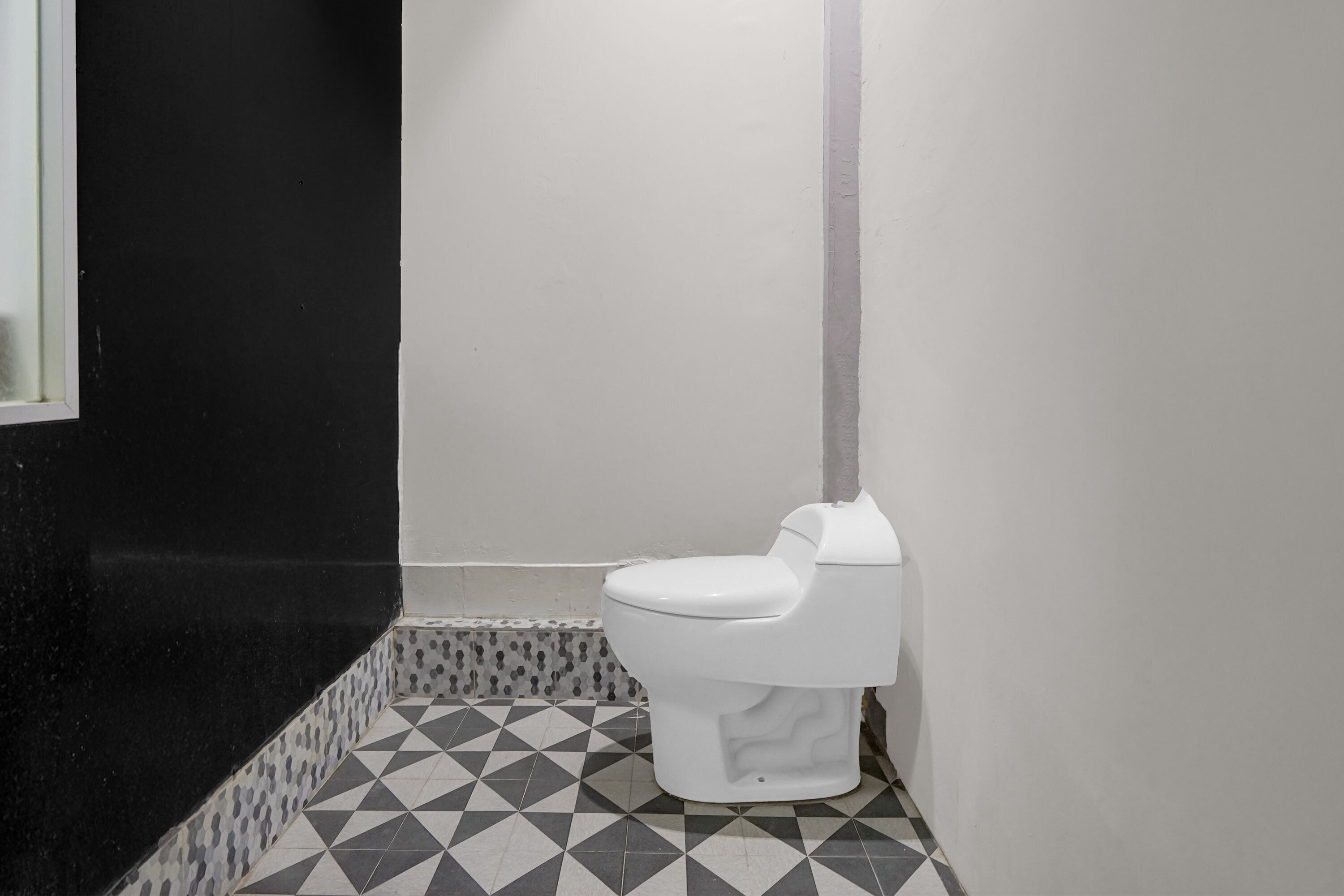 A bathroom with a white toilet, black and white patterned floor tiles, and a black wall.