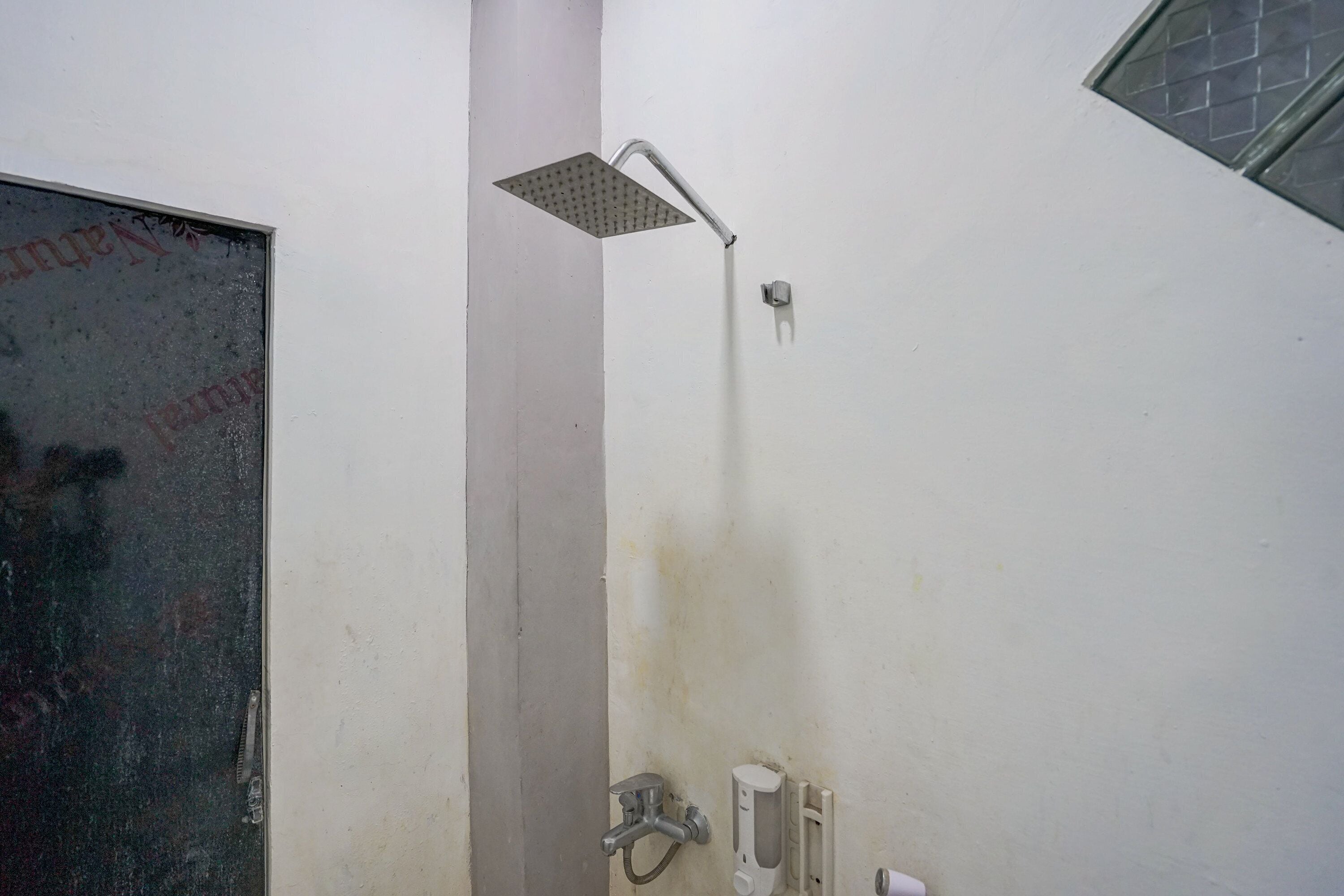 A shower with a square head, a wall-mounted control panel, and a door with a reflective surface.