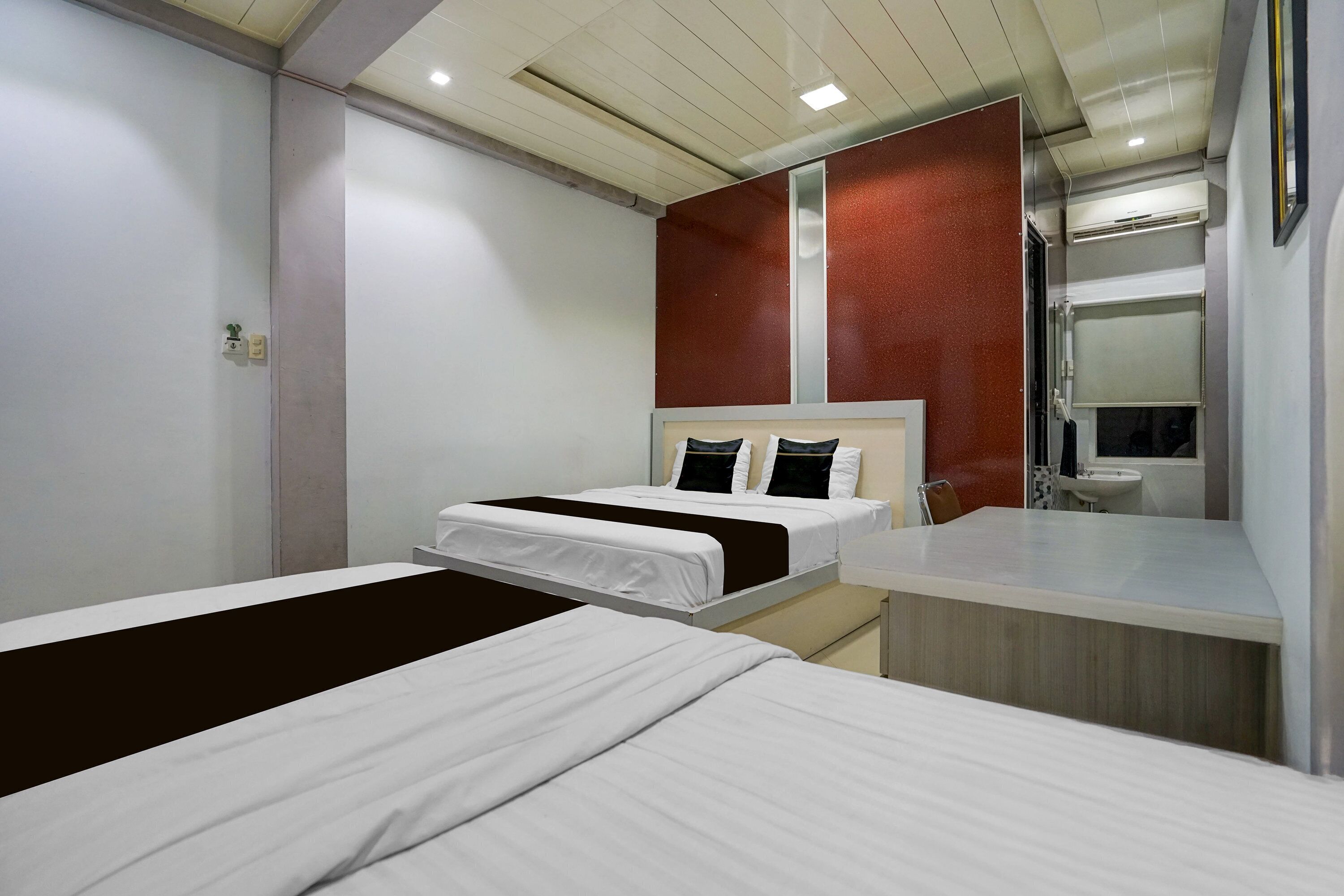 A hotel room with two beds, a large mirror, a small bathroom, and a wooden desk.