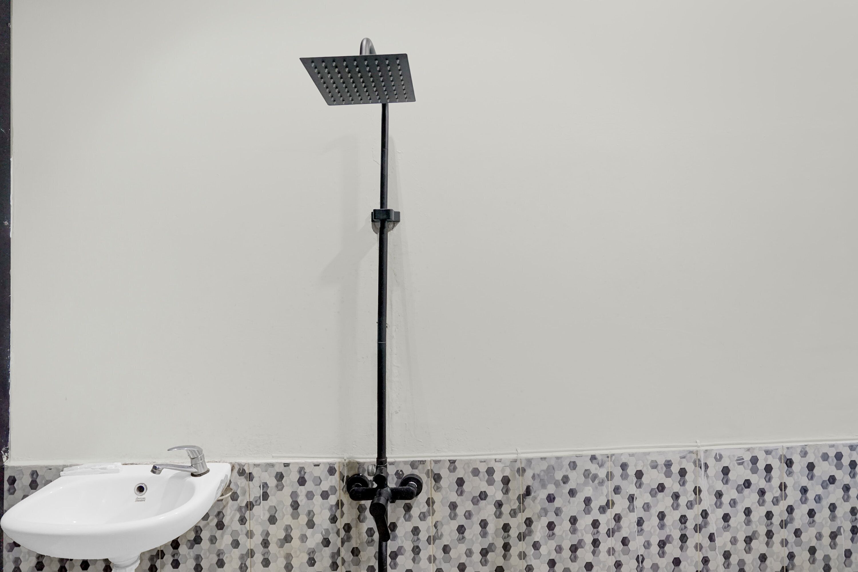 A bathroom with a white sink, a black showerhead, and patterned tile walls.