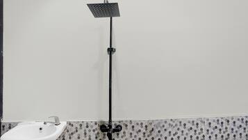 A bathroom with a white sink, a black showerhead, and patterned tile walls.