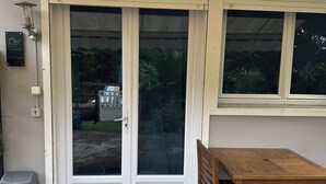A patio with a wooden table and chairs, a trash bin, and a door with a glass panel. - Sweet Pea F2 flirtatious in the countryside (Fort de France)