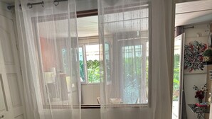 A bedroom with a bed, a window with sheer curtains, a patterned bedspread, and a view of the outdoors. - Sweet Pea F2 flirtatious in the countryside (Fort de France)