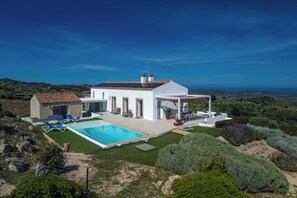 Una villa moderna con piscina, area relax esterna e vista sul paesaggio circostante.