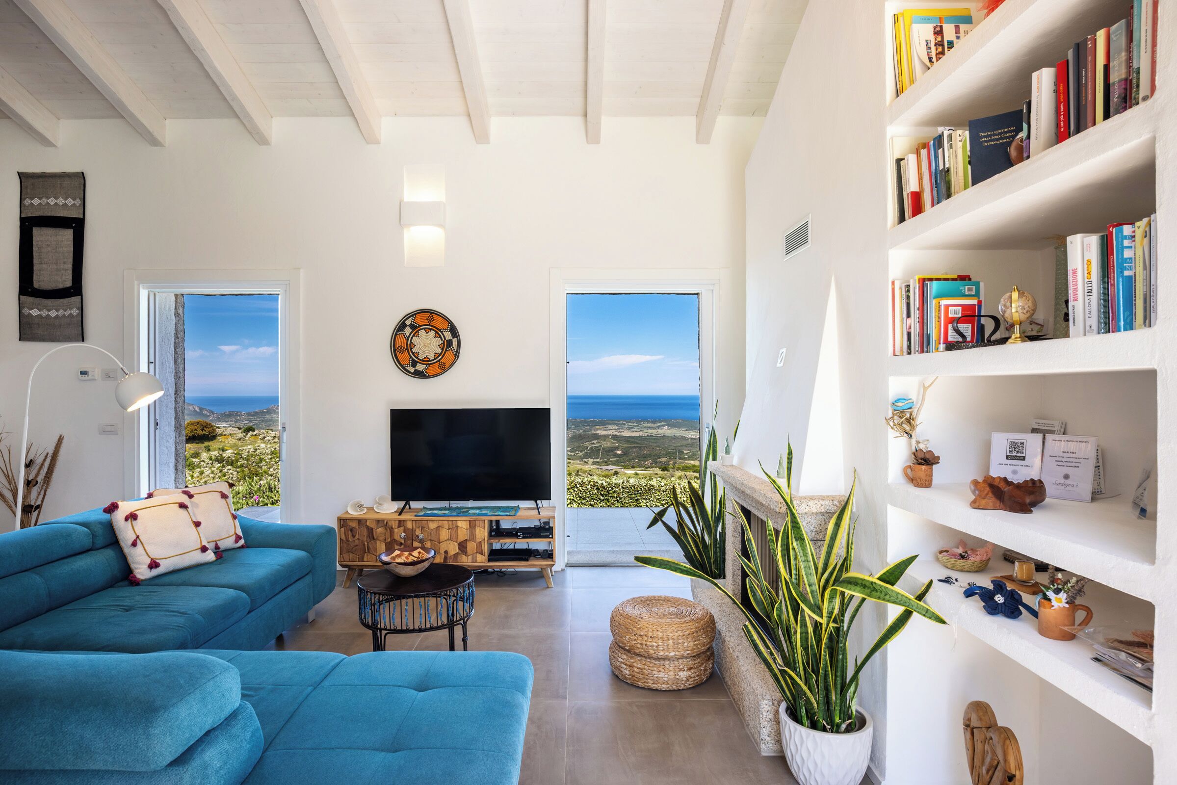 Een ruime woonkamer met een grote televisie, een bank, een boekenkast en uitzicht op zee.