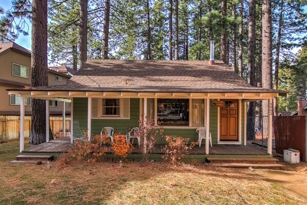 A single-story house with a porch, surrounded by tall trees.