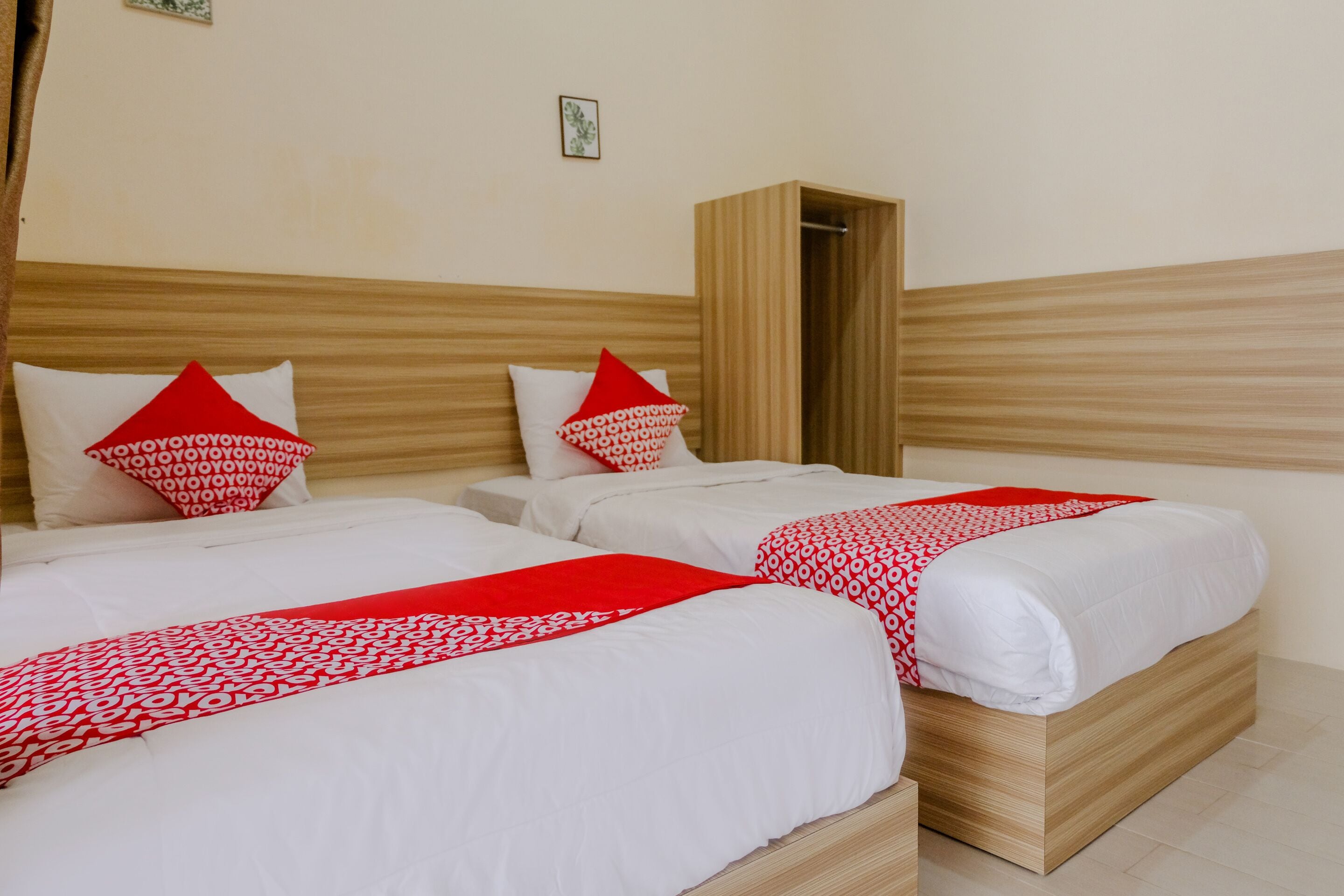 Une chambre d’hôtel avec deux lits, chacun agrémenté de draps blancs et de touches de couleur rouge, d’une tête de lit en bois et d’une petite fenêtre.