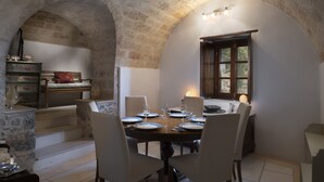 Un coin repas agrémenté d’une arche en pierre, d’une table en bois dressée pour quatre personnes et offrant une vue sur l’extérieur par une fenêtre.