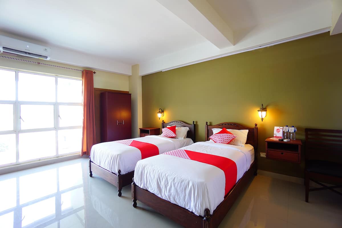 A hotel room with two beds, a window with curtains, a nightstand with a lamp, and a wooden chair.