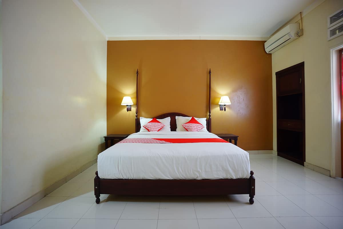 A neatly made bed with white linens and red pillows, two bedside lamps, and a wooden headboard.