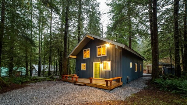 A cabin with a wooden deck and a gravel path leading to it, surrounded by a dense forest. - 66SL - Hot Tub - WiFi - 3+ Bedroom - Sleeps 10 Home by RedAwning (Deming)