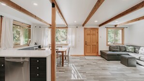 Une cuisine moderne dotée d’un îlot central, de poutres en bois au plafond et d’un coin repas avec une table et des chaises.
