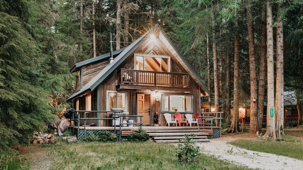 Une cabane dotée d’un balcon, d’une véranda avec des chaises et surplombant une forêt.