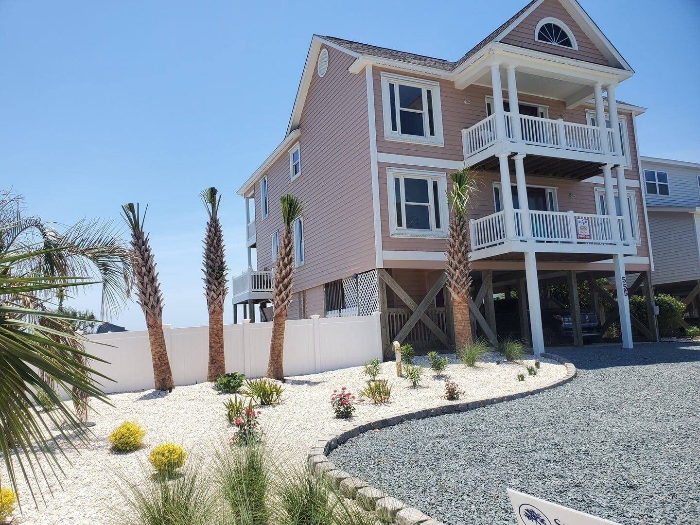 A multi-story beachfront building with balconies, a gravel driveway, and palm trees.