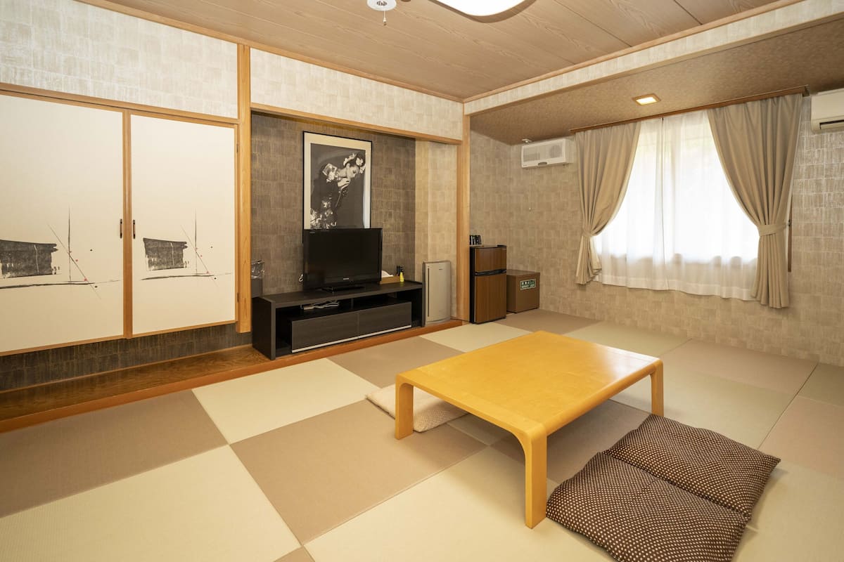 A traditional Japanese-style room with tatami flooring, a low wooden table, a television, and sliding doors.