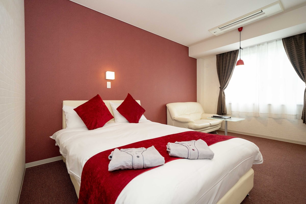 A hotel room with a large bed, red pillows, a red throw blanket, and a chair.