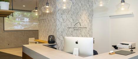 A modern hotel reception area with a marble-patterned wall, a large desk with an Apple iMac, and pendant lighting.