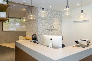 Un área de recepción de hotel moderna con una pared de diseño de mármol, un mostrador amplio con un Apple iMac e iluminación colgante.