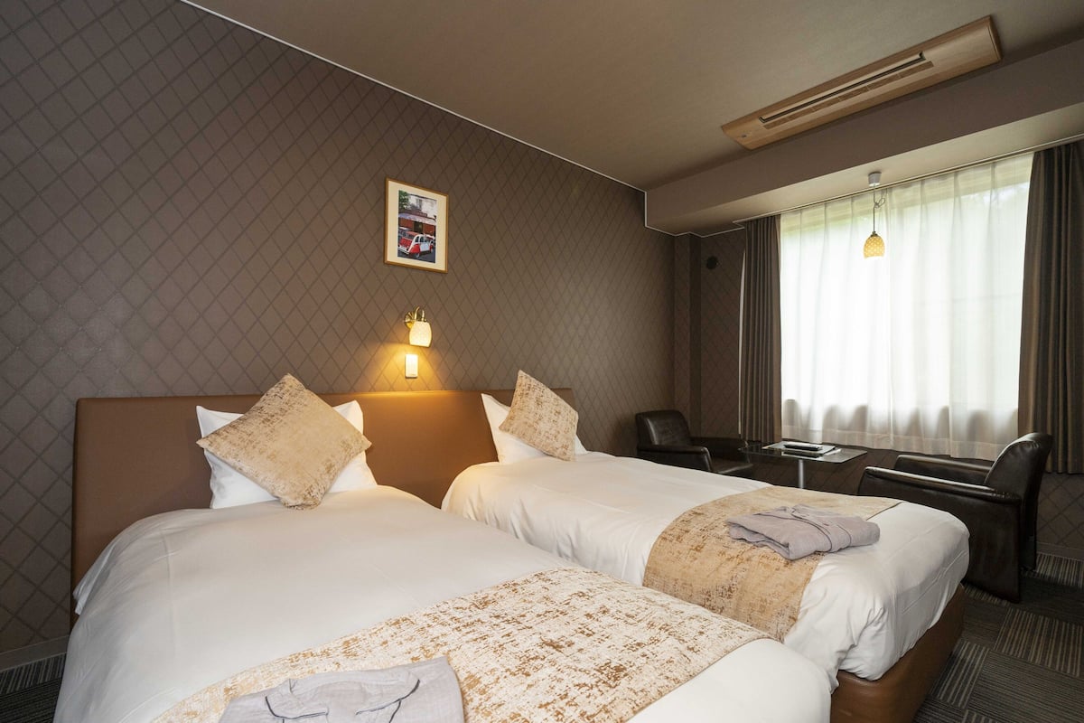 A hotel room with two beds, a desk, a chair, and a window with curtains.