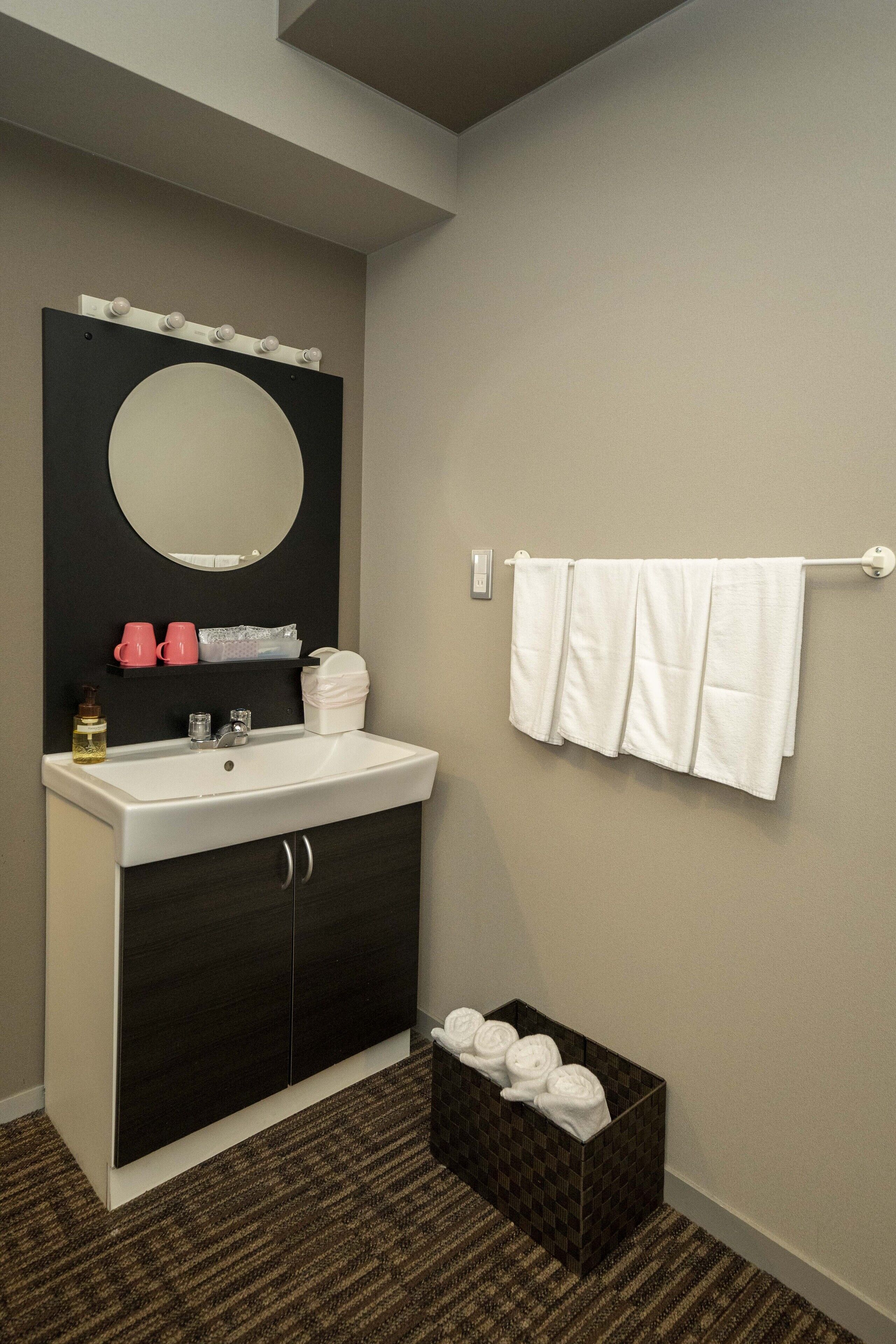 A bathroom with a sink, mirror, towel rack, and a box of towels.