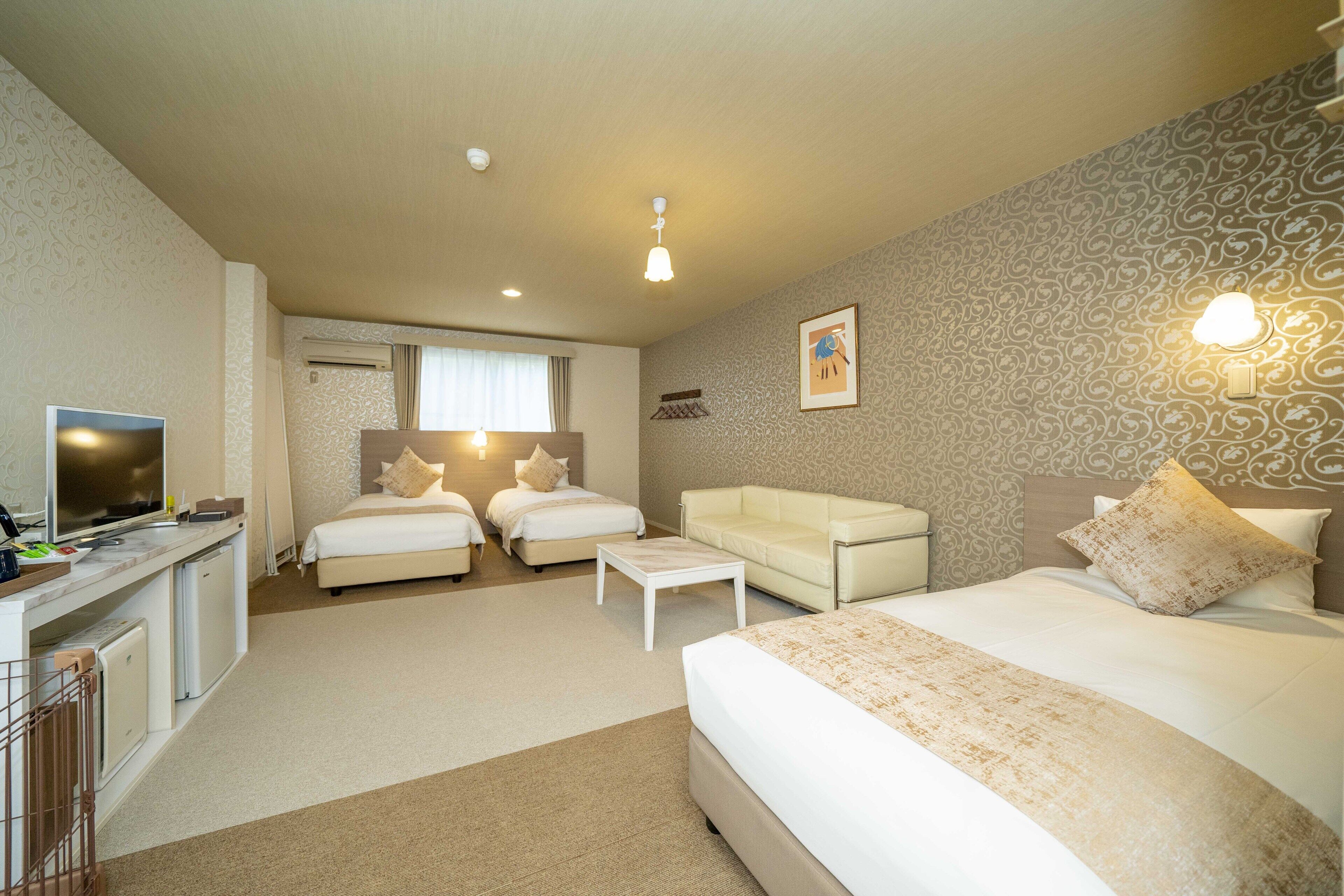 A hotel room with a bed, two sofas, a desk with a TV, and a small kitchenette.