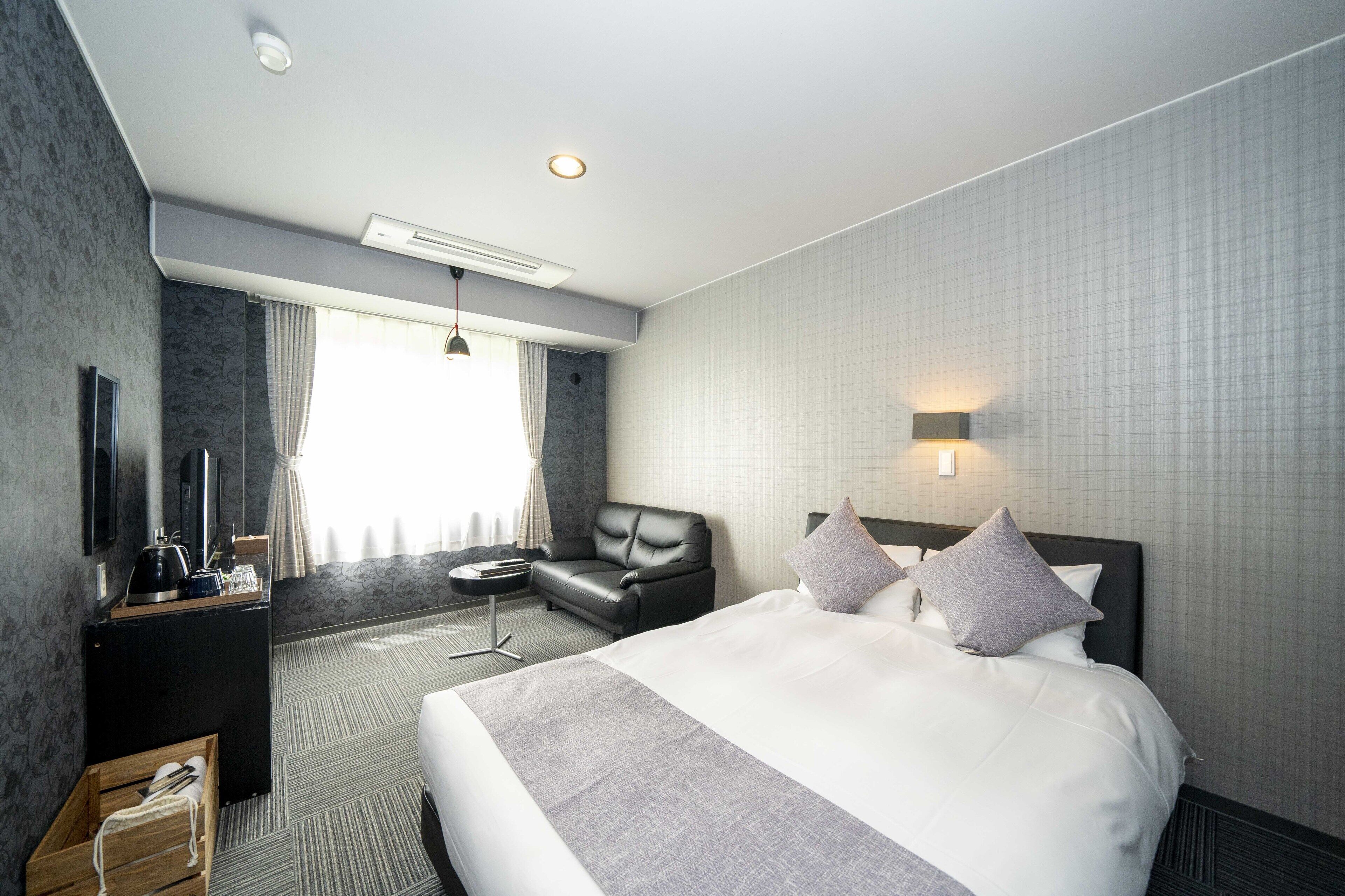 A hotel room with a large bed, a desk with a flat-screen TV, a leather armchair, and a small table.