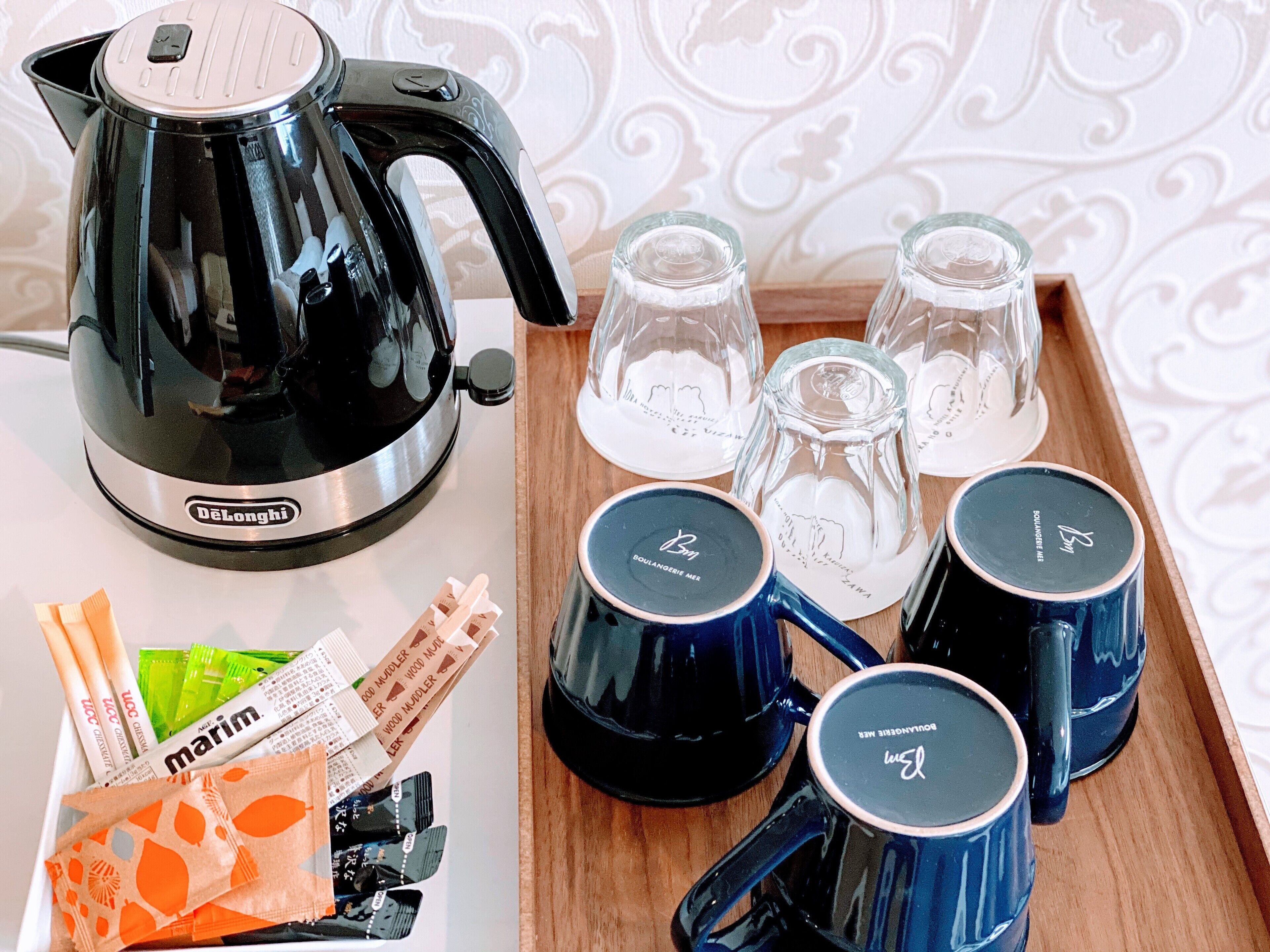 A tray with a black DeLonghi electric kettle, four blue mugs with "Boulangerie" text, and several packets of coffee and tea.